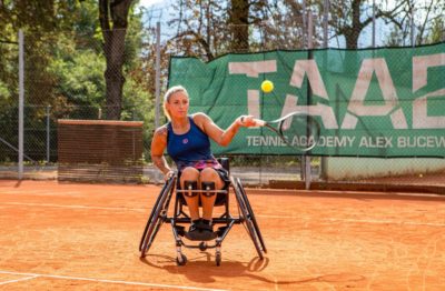 Eine junge, sportliche Frau spielt in ihrem Sportrollstuhl professionell Rollstuhltennis auf dem Tennisplatz.