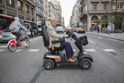 Ein Mann überquert die Straße mit seinem Elektromobil von Invacare